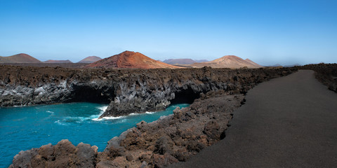 Los Hervideros lava caves (cliffs) in Lanzarote, Canary islands, Spain with Montana Bermeja volcano in the background