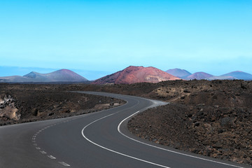 Winding road on Lanzarote, Canary islands, Spain, with multiple red volcanoes in the background