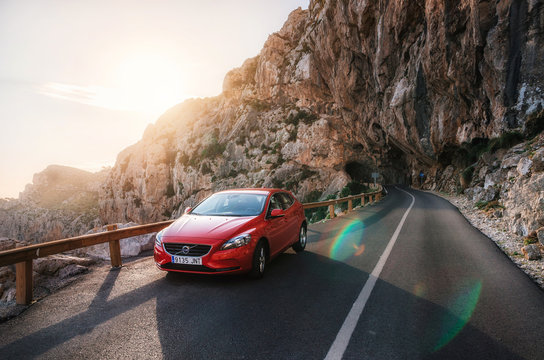 Red car Volvo V40 traveling on the mountain serpentine through a tunnel of a rock along the coast of Majorca against the sunshine. Roadtrip around Mallorca island