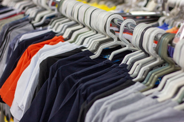 Many different colorful clothes on a hanging rack in the retail shop store. Soft selective focus photography