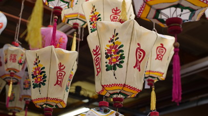 Fototapeta premium A group of old traditional Chinese lanterns hangs in a dusty antique warehouse, they're full of the beautiful script, colour & patterns. 
