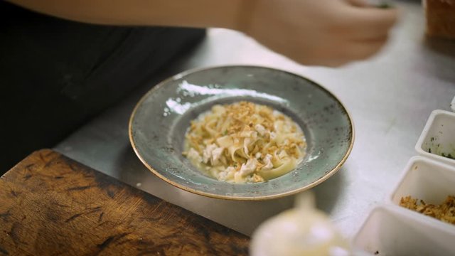 Close up of male chef hands decorated pappardelle in the plate ready to serve in the italian kitchen restaurant. Handheld shot of pappardelle with friend onions and greenery