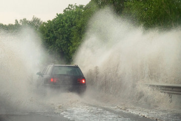 Car runs into big puddle at heavy rain, water splashing over the car. Car driving on asphalt road at thunder storm. Dangerous driving conditions