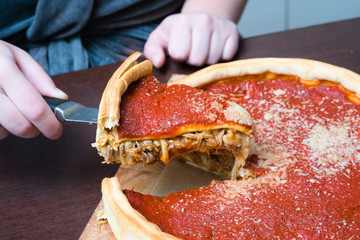 Top view of Chicago pizza. Woman hands cutting Chicago style deep dish italian cheese pizza with...