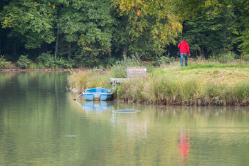 Fototapeta na wymiar un homme en rouge marche au bord de l'eau et regarde une barque bleue
