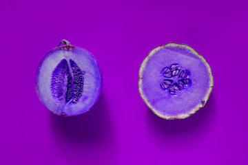 Cantaloupe sliced in half with whole cantaloupe isolated on purple neon background