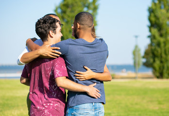 Happy old friends hugging outside. Young men and woman standing in circle on grass and embracing each other. Close friendship or bonding concept