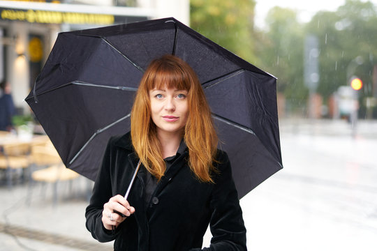 Ginger caucasian woman red hair holding an umbrella in the rain
