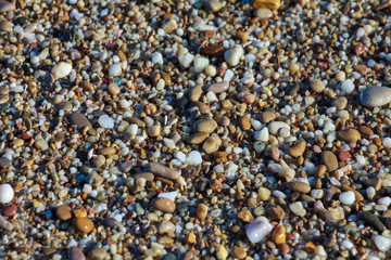 sea pebbles colored granite on the beach background stones. The shore of the beach with sand and pebbles washed by the waves of the sea.