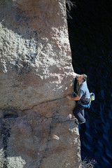 a young man climbs a steep cliff on the background of the lake. summer day. vertical shot