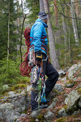 climber in a blue jacket with his equipment in the hands and on the belt, ready to climb. on the background of the forest. autumn