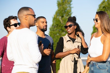 Multiethnic friends chatting over bottle of beer outside. People standing in circle, drinking bottled beer, talking, laughing. Hanging out concept