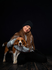 A red-haired girl of ten years old plays with a beagle puppy sitting on a dark wooden floor...