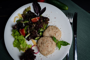Chicken cutlets steamed with vegetables on a white plate. 
