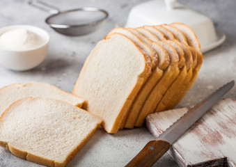 Cut of fresh loaf of white bread with flour and butter on light kitchen table background with chopping board and bread knife. Traditional bakery heritage.