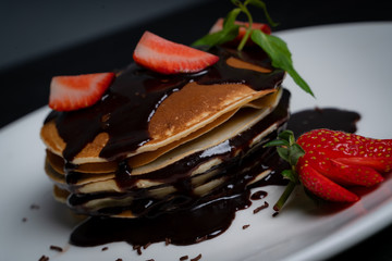 Pancakes with chocolate sauce and strawberry slices on a white plate 