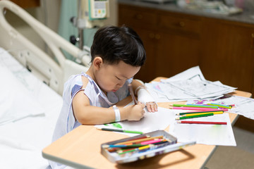 The patient boy is painting the paper with a color pencil in the hospital.