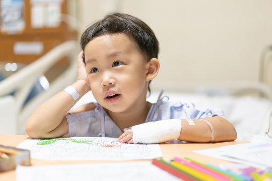 The patient boy is painting the paper with a color pencil in the hospital.