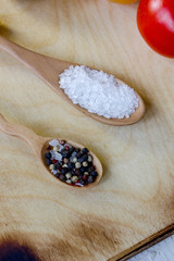 Sea salt and black pepper in wooden spoons over wooden kitchen board.
