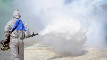 Obraz premium Rear view of outdoor healthcare worker using fogging machine spraying chemical to eliminate mosquitoes and prevent dengue fever at general location in community