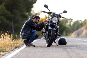 Young man biker checking his motorbike before driving it on the road. - obrazy, fototapety, plakaty