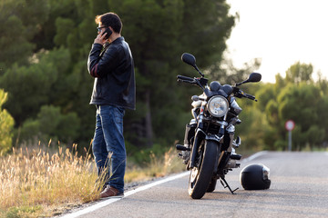 Man biker talking on the phone to the insurance of his motorcycle after having suffered a breakdown...