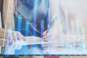 A woman hands writing information about stock market in notepad. Forex chart holograms in front. Concept of research. Double exposure