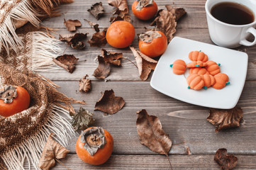 Fall flatlay with checkered plaid, coffee, persimmons, pumpkin candies and dry leaves