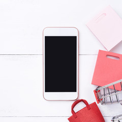 Abstract online shopping, mobile payment concept design element, colorful cart and paper bags on white wooden table background, top view, flat lay