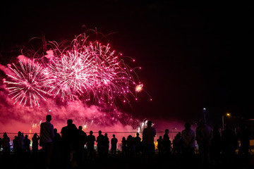 silhouettes of people watching fireworks in the background of bright red flashes in the night sky