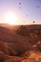 zonsopgangfoto in Cappadocië met luchtballonnen in de lucht boven zandheuvels en een meisje dat op de grond staat