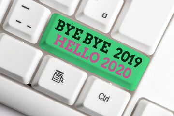 Handwriting text writing Bye Bye 2019 Hello 2020. Conceptual photo Starting new year Motivational message 2019 is over White pc keyboard with empty note paper above white background key copy space © A