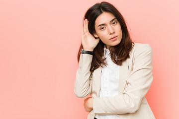 Young brunette business woman against a pink background trying to listening a gossip.