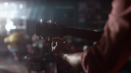 Close-up of a man tuning his acoustic guitar and starts to play in a dimly lit bar with a lens flare