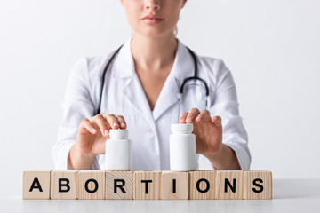 cropped view of doctor touching bottles on cubes with abortion letters