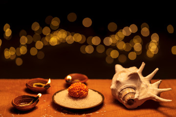 Diwali Festive Season. Diwali - also known as Festival of Lights. Religious traditional clay diya lit on a wooden surface decorated with flowers, rice grains, shankha for Hindu culture background.