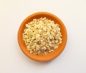 Raw Oats scattered in a clay bowl on white background. Oat flakes uncooked in ceramic plate isolated on white. Concept of healthy eating vegan food. 