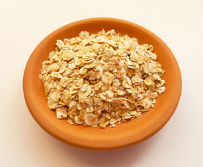 Raw Oats scattered in a clay bowl on white background. Oat flakes uncooked in ceramic plate isolated on white. Concept of healthy eating vegan food. 