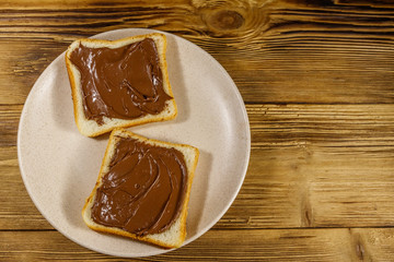 Two slices of bread with delicious chocolate hazelnut spread on wooden table. Top view