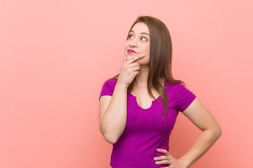 Young hispanic woman against a pink wall looking sideways with doubtful and skeptical expression.