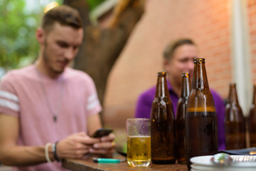 Happy man sitting and using phone outdoors while having beer focus on foreground