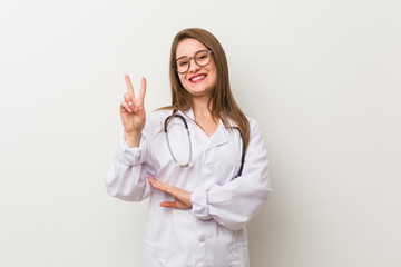 Young doctor woman against a white wall showing number two with fingers.