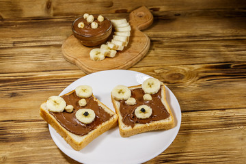 Two sweet sandwiches with delicious chocolate hazelnut spread and banana in shape of bear on wooden table