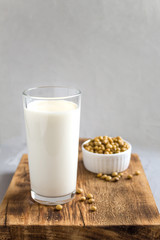 soy milk in a glass and beans on a wooden stand on a gray background. Side view, copy space. Vegetable milk, vegetarian food. The concept of healthy eating.