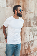 Young hipster man with beard wearing white blank t-shirt and blue jeans outdoor.