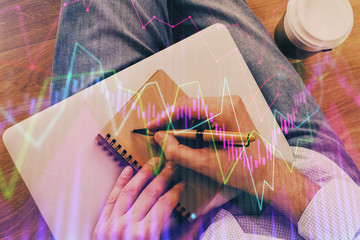 Double exposure of hands writing in notepad with stock market chart.