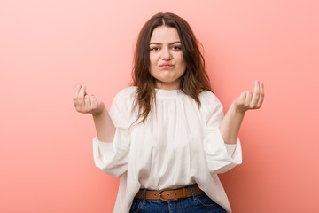 Young caucasian curvy woman standing against pink background