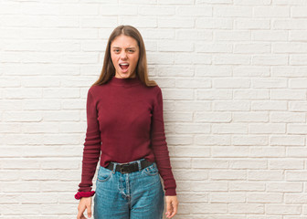 Young cool woman over a bricks wall screaming very angry and aggressive
