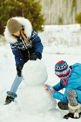 friends building a snowman. funny girls on a walk in the winter outdoors