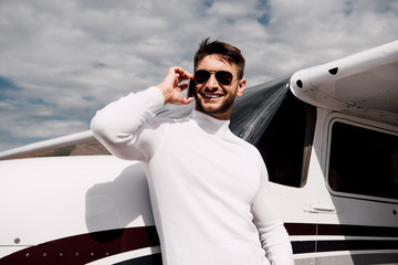 smiling bearded man in sunglasses talking on smartphone near plane